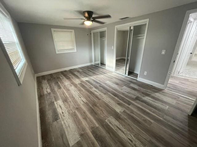 unfurnished bedroom with dark wood-type flooring, two closets, and ceiling fan