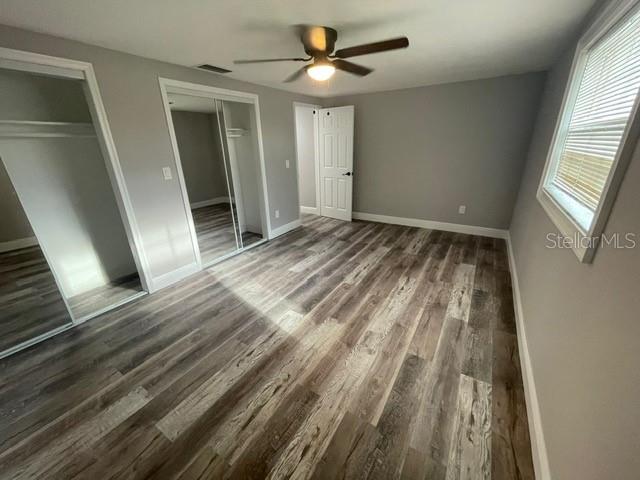 unfurnished bedroom with ceiling fan, multiple closets, and dark hardwood / wood-style flooring