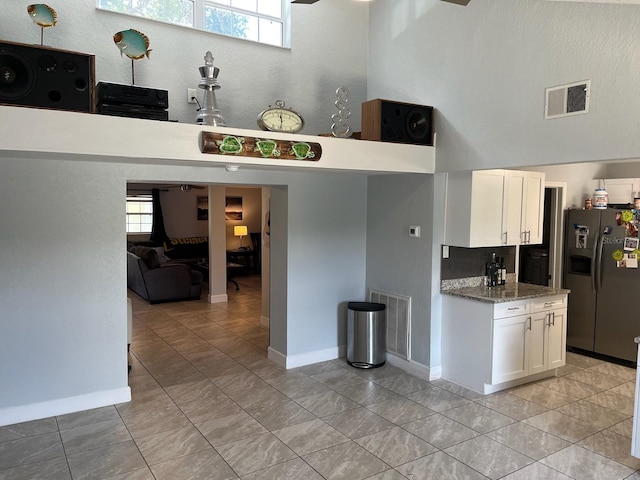 kitchen featuring light stone countertops, stainless steel refrigerator with ice dispenser, white cabinetry, and light tile patterned floors