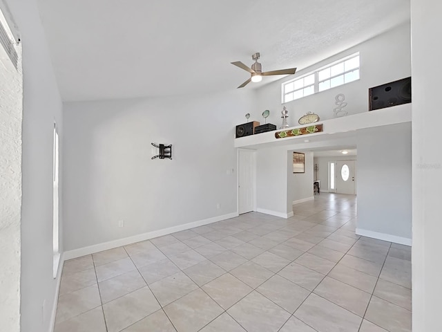 spare room with light tile patterned floors, a ceiling fan, baseboards, and a towering ceiling