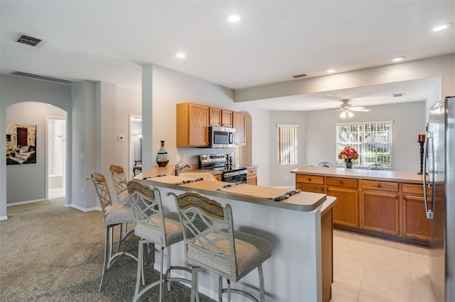 kitchen featuring appliances with stainless steel finishes, light carpet, a kitchen bar, kitchen peninsula, and ceiling fan