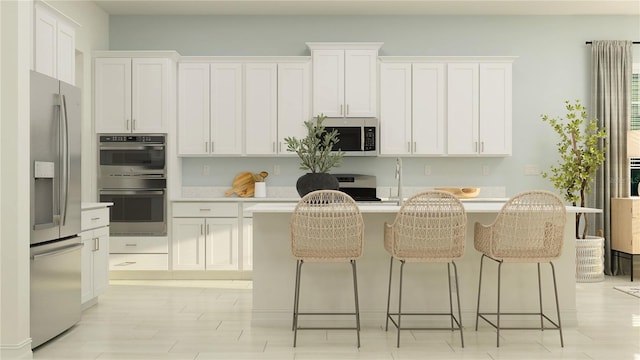 kitchen with stainless steel appliances, a center island with sink, white cabinetry, and a breakfast bar