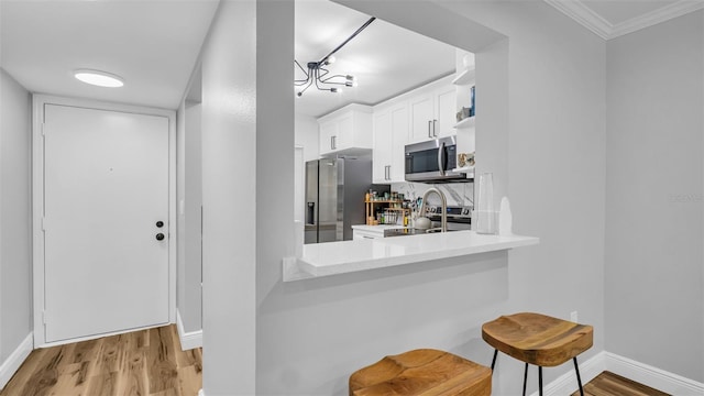 kitchen featuring ornamental molding, white cabinetry, appliances with stainless steel finishes, a breakfast bar area, and light wood-type flooring