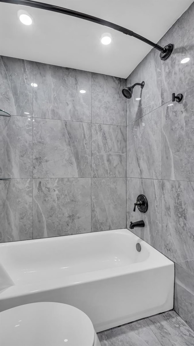 bathroom with tile walls, tiled shower / bath combo, and toilet