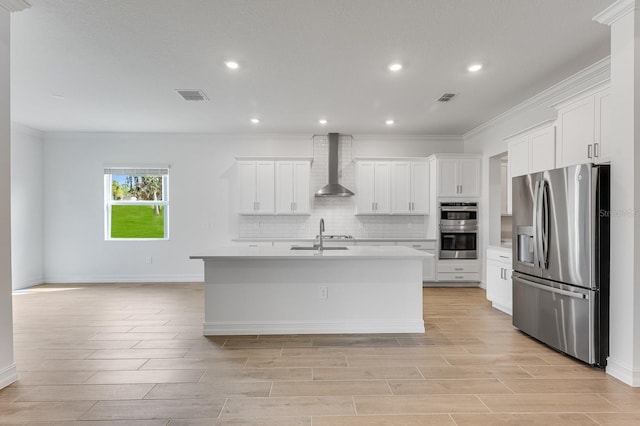 kitchen featuring white cabinets, appliances with stainless steel finishes, a kitchen island with sink, and wall chimney range hood