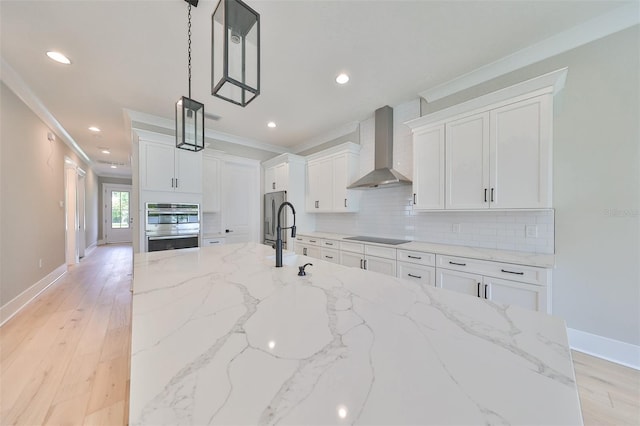 kitchen with white cabinets, light stone countertops, pendant lighting, and wall chimney range hood