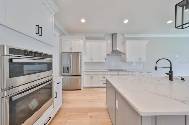 kitchen with light hardwood / wood-style flooring, stainless steel appliances, wall chimney range hood, and white cabinetry