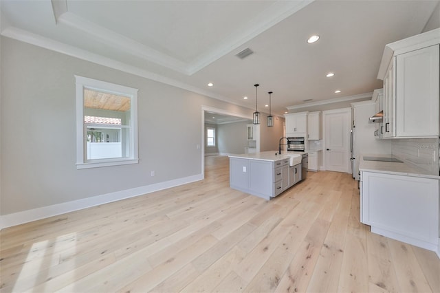 kitchen with decorative backsplash, light hardwood / wood-style floors, white cabinetry, pendant lighting, and a kitchen island with sink