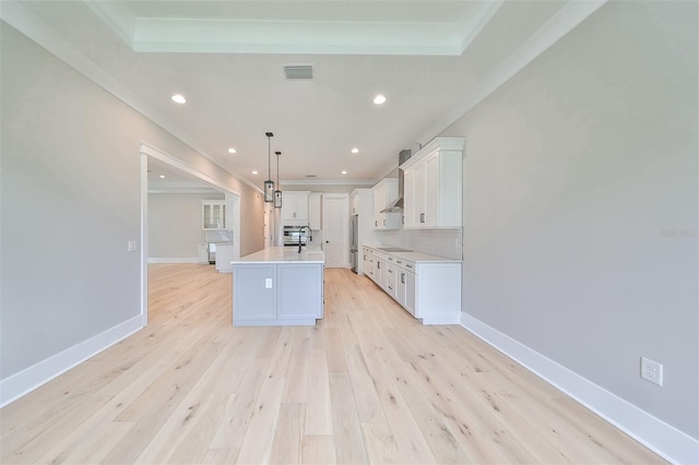 kitchen featuring an island with sink, white cabinets, stainless steel refrigerator, light wood-type flooring, and decorative light fixtures