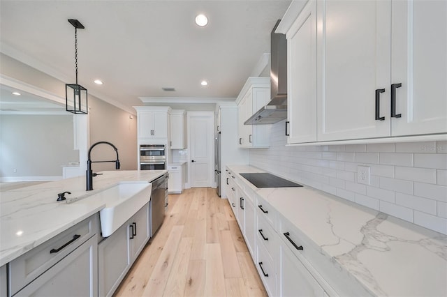 kitchen featuring hanging light fixtures, wall chimney exhaust hood, white cabinetry, and light stone counters