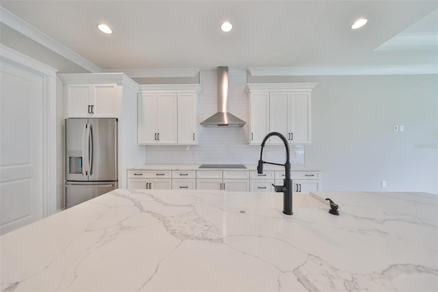 kitchen featuring black electric cooktop, stainless steel fridge, wall chimney range hood, and white cabinetry