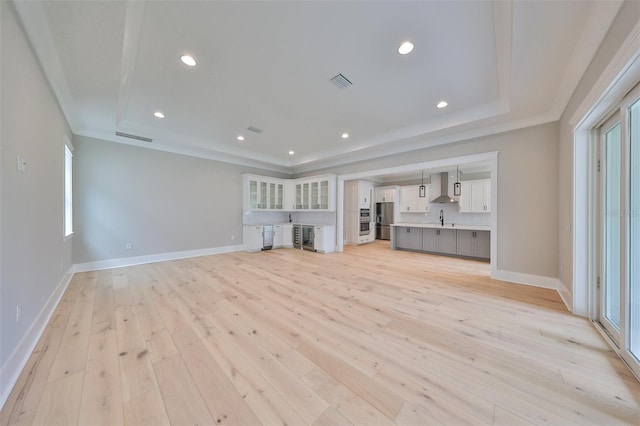 unfurnished living room featuring light wood-type flooring, a raised ceiling, and sink