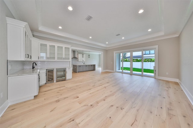 kitchen featuring white cabinets, sink, beverage cooler, a tray ceiling, and light hardwood / wood-style floors