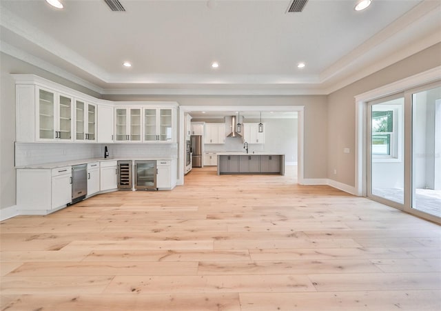 kitchen featuring beverage cooler, light hardwood / wood-style flooring, wall chimney range hood, white cabinetry, and stainless steel refrigerator