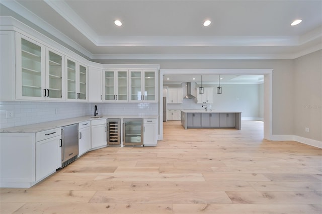 kitchen with light wood-type flooring, wall chimney exhaust hood, white cabinetry, and beverage cooler