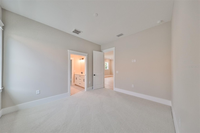 unfurnished bedroom with ensuite bath and light colored carpet