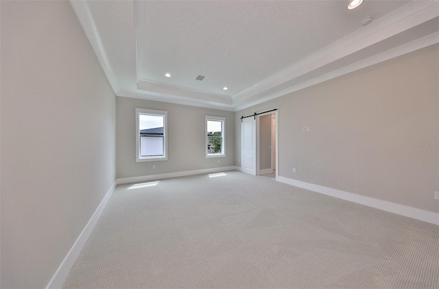 carpeted empty room with a barn door and a raised ceiling