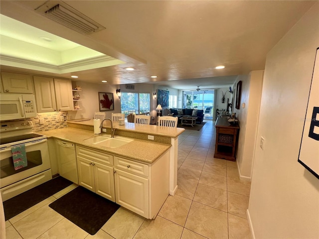 kitchen featuring light tile patterned floors, sink, kitchen peninsula, white appliances, and a tray ceiling