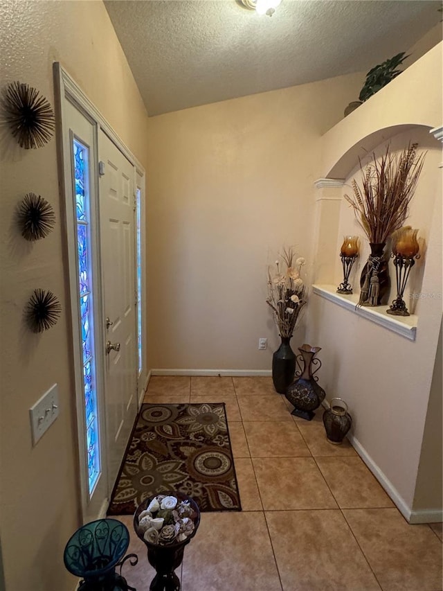 foyer featuring vaulted ceiling, a textured ceiling, and light tile patterned floors