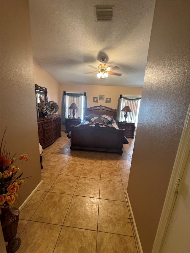 bedroom with ceiling fan, light tile patterned floors, and a textured ceiling