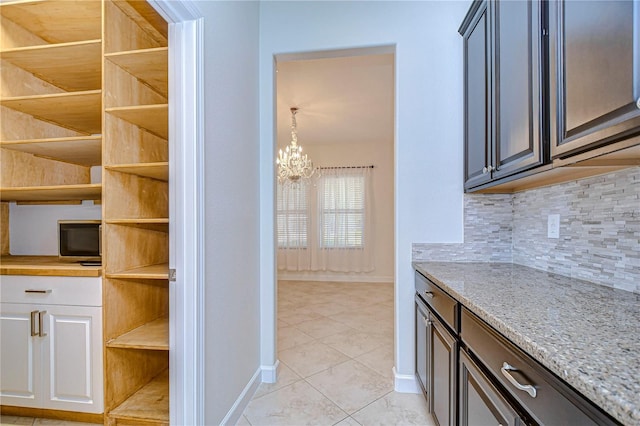 kitchen featuring dark brown cabinetry, light tile patterned flooring, decorative backsplash, a notable chandelier, and wood counters