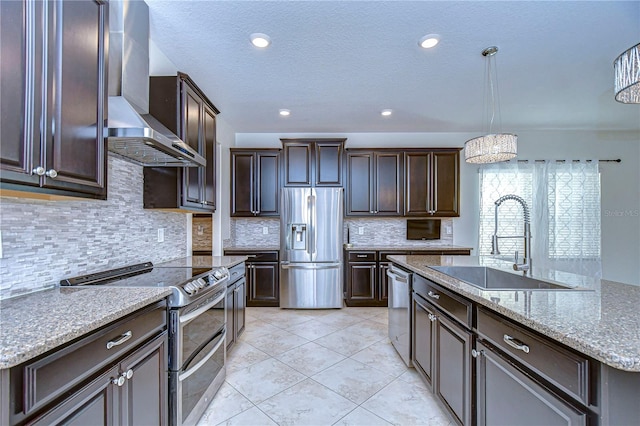 kitchen featuring dark brown cabinets, sink, wall chimney range hood, appliances with stainless steel finishes, and decorative light fixtures