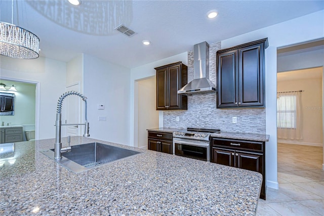 kitchen with light stone countertops, electric range, dark brown cabinets, sink, and wall chimney range hood