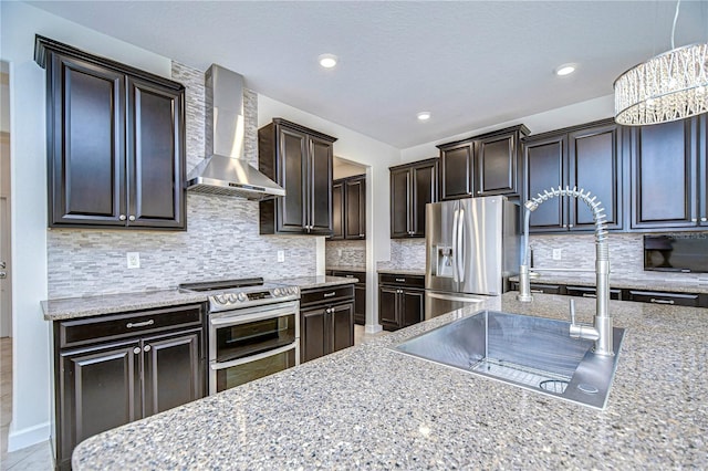 kitchen with pendant lighting, appliances with stainless steel finishes, tasteful backsplash, and wall chimney range hood