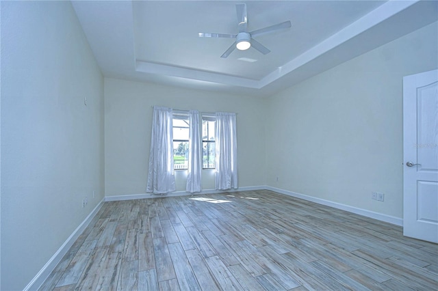 unfurnished room featuring ceiling fan, light hardwood / wood-style flooring, and a raised ceiling