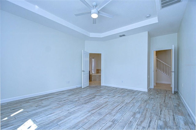 interior space with light wood-type flooring, ceiling fan, and a raised ceiling