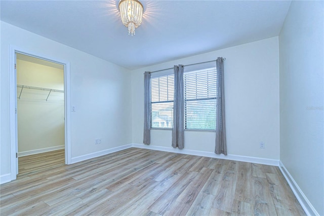 unfurnished bedroom featuring light hardwood / wood-style flooring, a chandelier, a closet, and a spacious closet