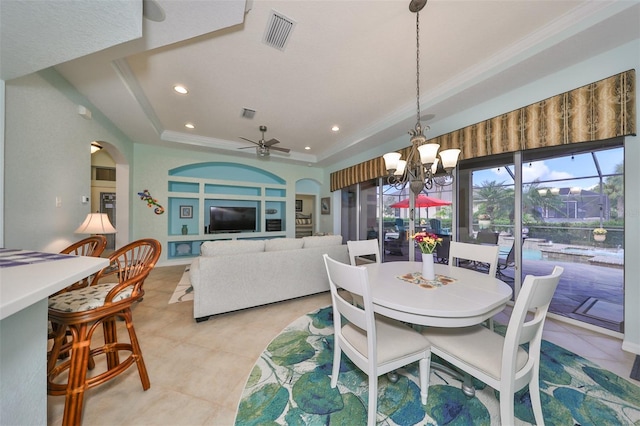 dining room with ceiling fan with notable chandelier, a tray ceiling, ornamental molding, and light tile patterned flooring