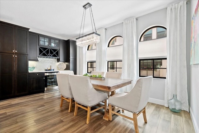 dining room featuring light hardwood / wood-style floors, beverage cooler, a healthy amount of sunlight, bar area, and a notable chandelier