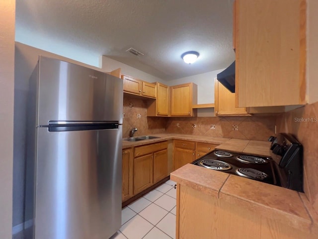 kitchen with electric range, sink, stainless steel refrigerator, backsplash, and light brown cabinetry