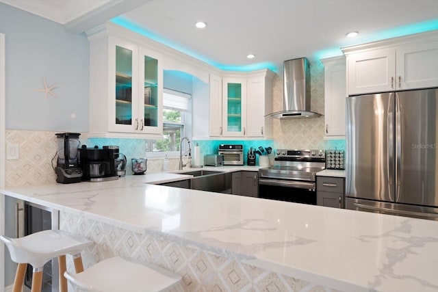 kitchen featuring sink, white cabinetry, wall chimney range hood, stainless steel appliances, and light stone countertops