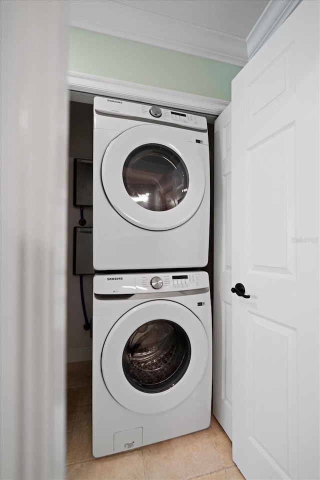 clothes washing area with crown molding, stacked washer and dryer, and light tile patterned floors