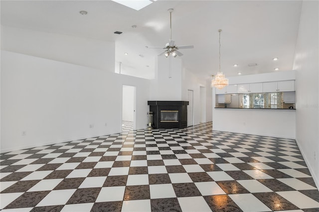 unfurnished living room with ceiling fan with notable chandelier and high vaulted ceiling