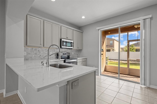 kitchen with gray cabinets, kitchen peninsula, appliances with stainless steel finishes, and tasteful backsplash