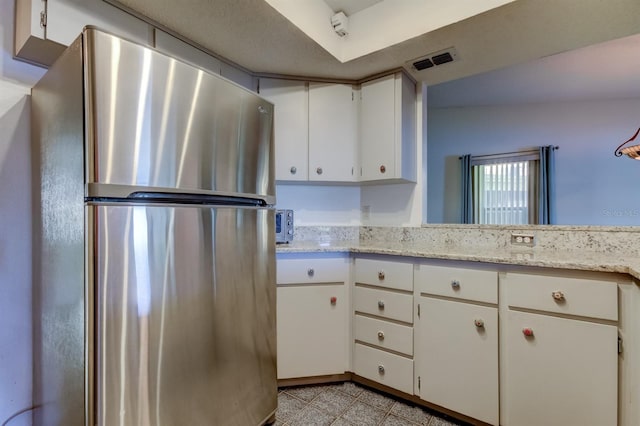 kitchen featuring white cabinets, stainless steel fridge, light stone counters, and lofted ceiling