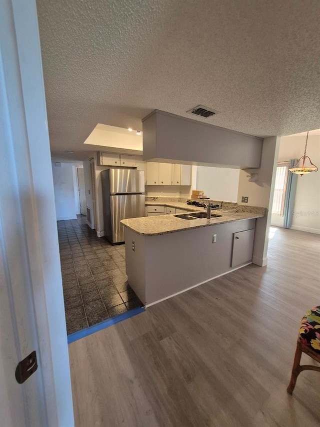 kitchen with kitchen peninsula, decorative light fixtures, white cabinets, and stainless steel refrigerator