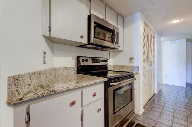 kitchen featuring appliances with stainless steel finishes, a textured ceiling, white cabinetry, and light tile patterned flooring