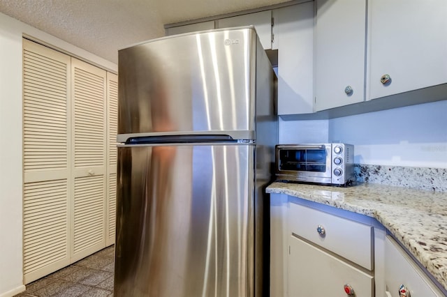 kitchen with stainless steel refrigerator, white cabinetry, light stone countertops, and a textured ceiling