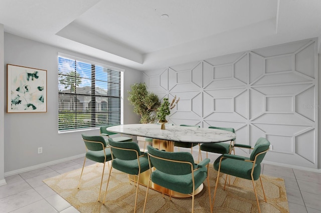 dining space featuring light tile patterned floors, a tray ceiling, baseboards, and an accent wall