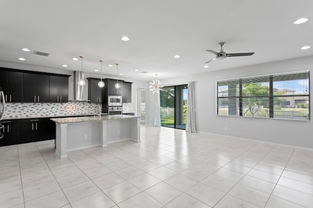 kitchen featuring light tile patterned flooring, wall chimney range hood, stainless steel appliances, and dark cabinetry