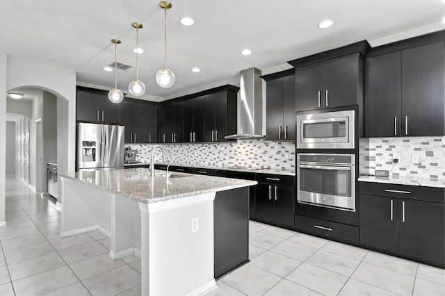 kitchen with a sink, wall chimney exhaust hood, dark cabinetry, stainless steel appliances, and visible vents