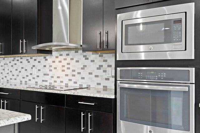 kitchen with wall chimney exhaust hood, tasteful backsplash, dark cabinetry, and appliances with stainless steel finishes