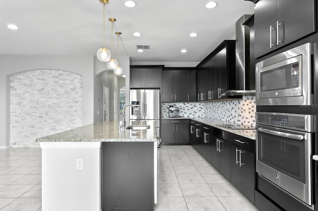 kitchen with backsplash, hanging light fixtures, sink, an island with sink, and appliances with stainless steel finishes