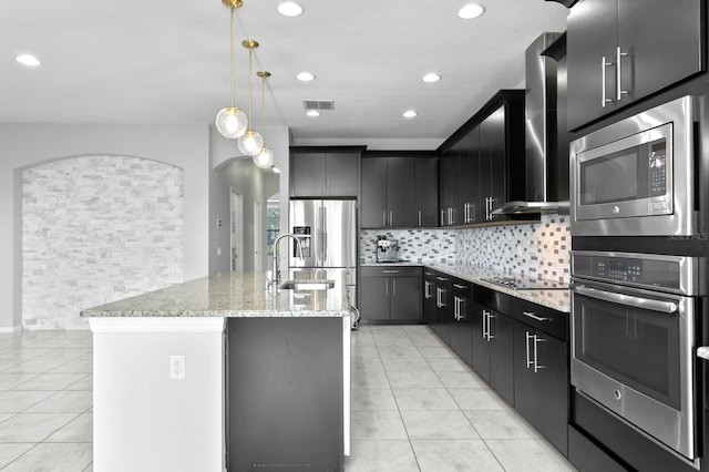 kitchen with light tile patterned flooring, a kitchen island with sink, a sink, and appliances with stainless steel finishes