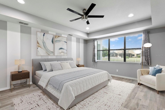 bedroom with a raised ceiling, light hardwood / wood-style flooring, and ceiling fan