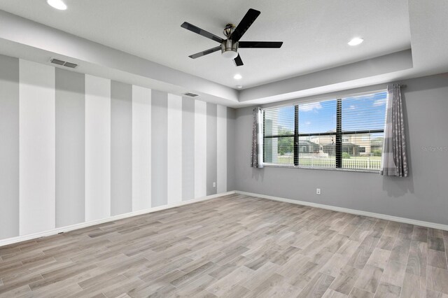 spare room featuring a tray ceiling, ceiling fan, and light hardwood / wood-style flooring